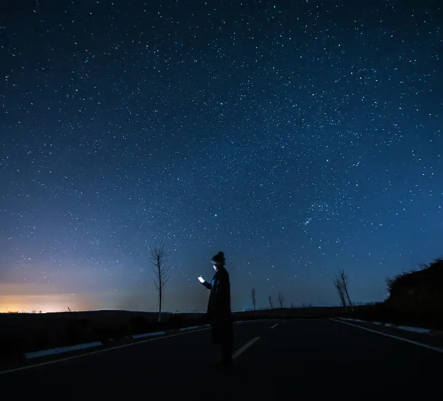 Mujer usando un teléfono inteligente bajo un cielo estrellado por la noche