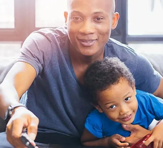 Person taking a selfie with a child sitting close, both looking at the camera.