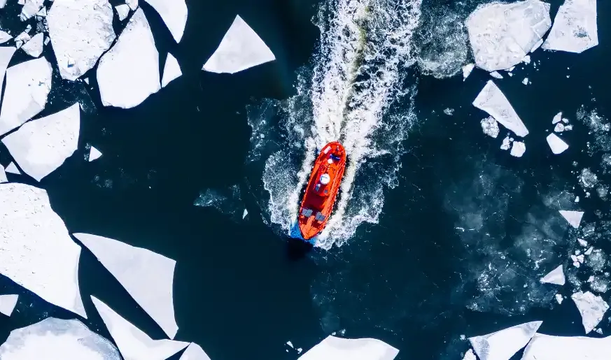 An aerial view of a red research vessel navigating through dark icy water