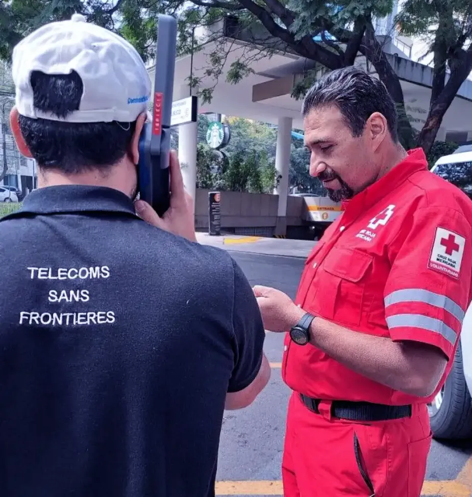 A humanitarian worker from the Red Cross speaks with a telecommunications technician outdoors