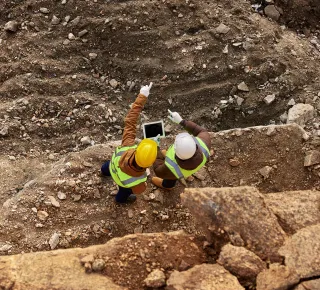 Top view shot of two industrial workers wearing reflective jackets standing on mining worksite outdoors using digital tablet