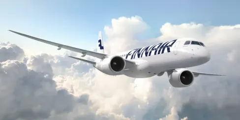 Finnair aircraft flying above clouds in a bright blue sky.
