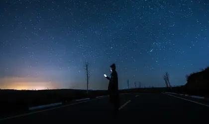 Mujer usando un teléfono inteligente bajo un cielo estrellado por la noche