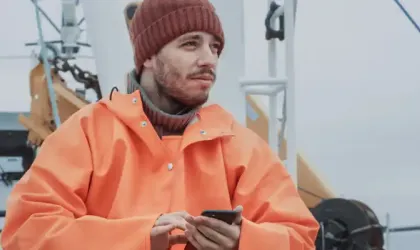 Pêcheur décontracté habillé utilisant le téléphone portable tout en voyageant sur le bateau