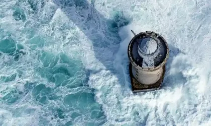 Aerial view of the Créac’h Lighthouse during a storm, with strong waves and rough seas.